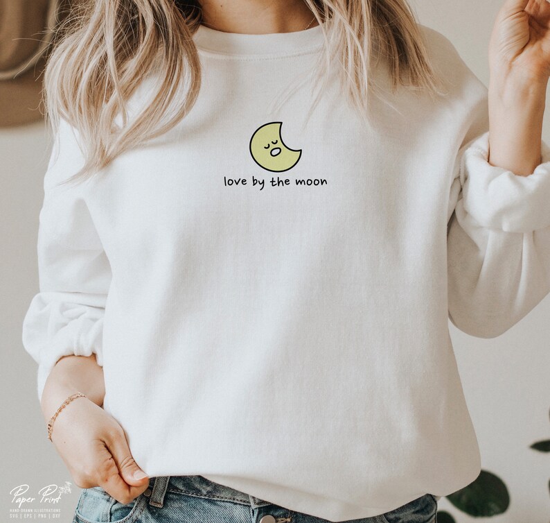 May include: White sweatshirt with a yellow crescent moon graphic and the text "love by the moon".