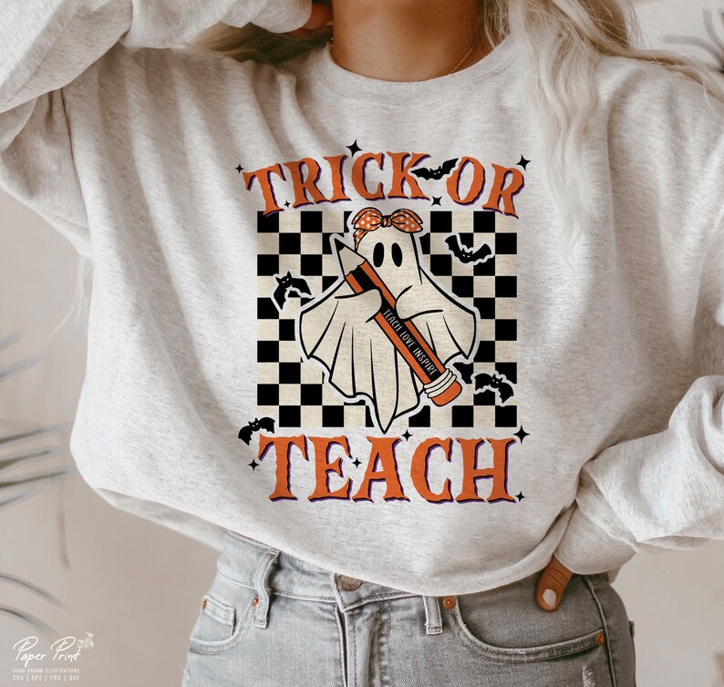 Op de afbeelding: Een grijs sweatshirt met een zwart-wit geruite achtergrond. Een geest met een rode strik en een potlood waarop "Teach Love Inspire" staat, houdt het potlood vast. De tekst "Trick or Teach" is op het sweatshirt gedrukt.