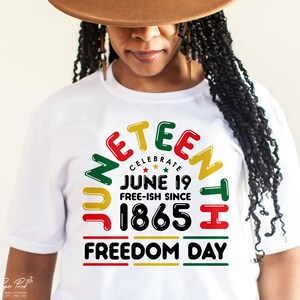 May include: White t-shirt with a graphic design that says "Juneteenth Celebrate June 19 Free-ish Since 1865 Freedom Day". The graphic is in a rainbow of colors, red, yellow, green, and black.