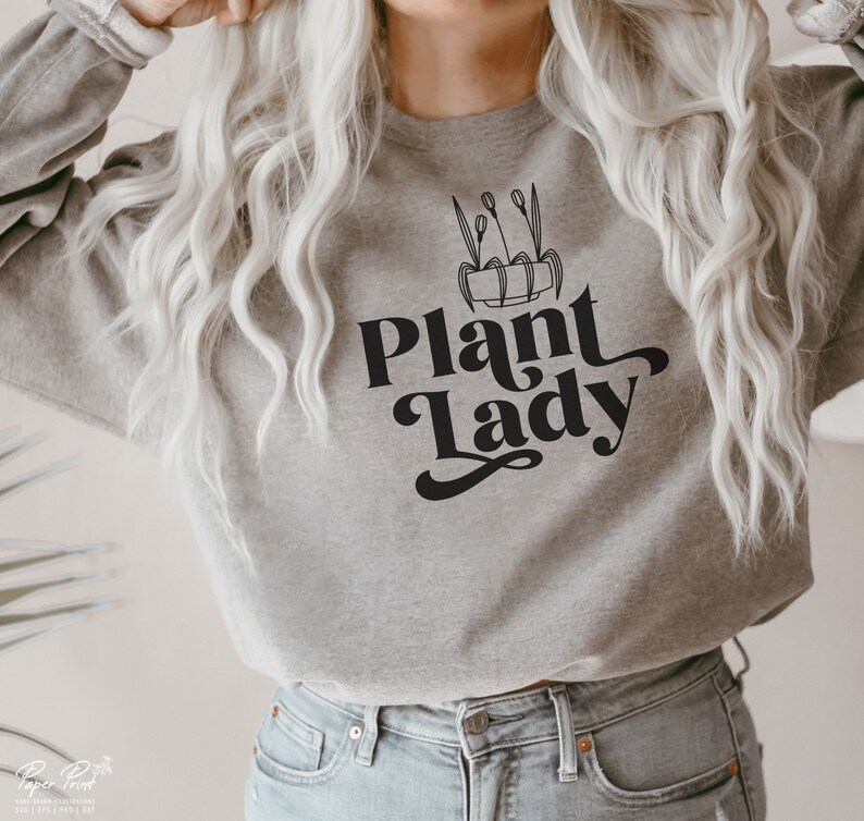 May include: A gray sweatshirt with the text "Plant Lady" in black script font. A black and white illustration of a potted plant with leaves is above the text.