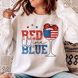 K&ouml;nnte beinhalten: Wei&szlig;es Sweatshirt mit einem roten, wei&szlig;en und blauen Weinglas-Motiv und dem Text "Red Wine & Blue".