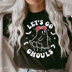 May include: Black t-shirt with a white graphic of a ghost wearing a red bandana and the text "Let's Go Ghouls".
