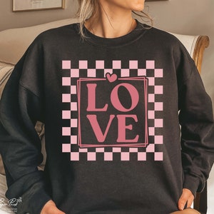 May include: Black sweatshirt featuring a pink checkered pattern and the word "LOVE" in a pink box.