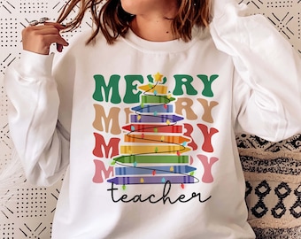 May include: White sweatshirt with a colorful graphic of a Christmas tree made of books. The words "MERRY MERRY MERRY" are stacked above the tree, and "teacher" is written below. The tree is decorated with lights and a star.