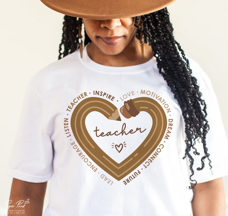 Pu&ograve; includere: Maglietta bianca con un disegno di matita marrone a forma di cuore. La matita &egrave; disegnata con un contorno marrone e ha una gomma marrone. Le parole "teacher" sono scritte al centro del cuore. Le parole "lead, encourage, listen, teacher, inspire, love, motivation, dream, connect, future" sono scritte in cerchio attorno al cuore.