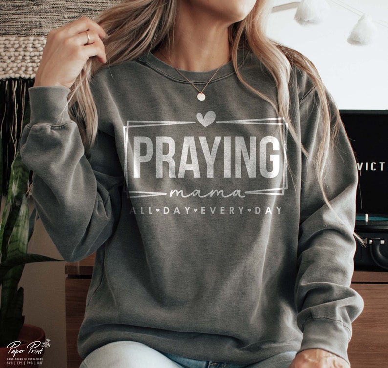 May include: A gray sweatshirt with the text "Praying mama all day every day" in white lettering. The text is inside a white rectangle with a heart at the top.