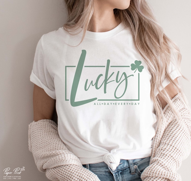May include: White t-shirt with a green shamrock and the text "Lucky" in a green cursive font. The text "All Day Every Day" is written in smaller font below the word "Lucky".