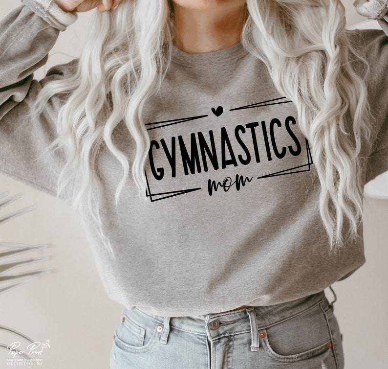 May include: A gray sweatshirt with the words "GYMNASTICS mom" in black, framed by a black rectangle and a small heart above the word "GYMNASTICS". The sweatshirt is worn with blue jeans.