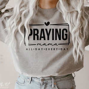 May include: Gray sweatshirt with black text that reads "Praying mama all day every day" with a heart symbol between each word.