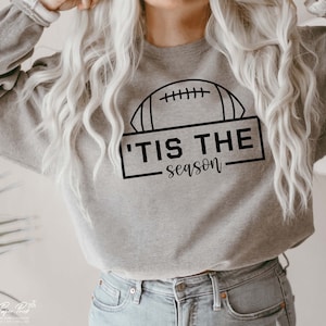 May include: A gray sweatshirt with a black outline of a football and the text 'Tis the season'.