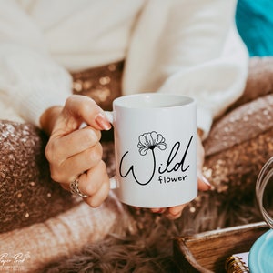 May include: White ceramic mug with a black design of a flower and the text "Wild flower".