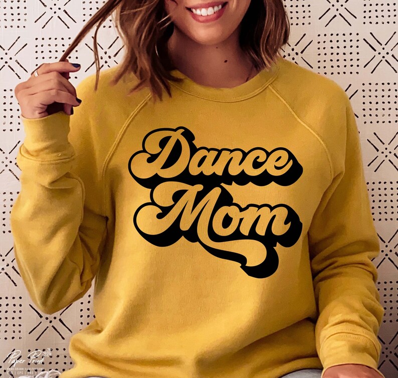 Peut inclure: Un sweat-shirt jaune moutarde avec le texte "Dance Mom" dans une police noire r&eacute;tro.