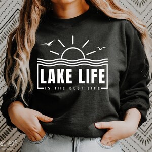 May include: Black sweatshirt with a white graphic that reads "LAKE LIFE IS THE BEST LIFE." The design includes a sun, waves, and two birds. The sweatshirt is a crew neck style.