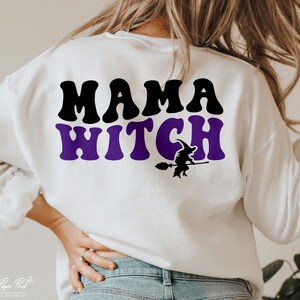 Pu&ograve; includere: Felpa bianca con il testo "Mama Witch" in lettere nere e viola. Sotto il testo c'&egrave; una silhouette di una strega che cavalca una scopa.