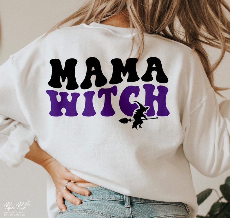 Pu&ograve; includere: Felpa bianca con il testo "Mama Witch" in lettere nere e viola. Sotto il testo c'&egrave; una silhouette di una strega che cavalca una scopa.