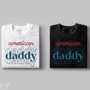 Puede incluir: Dos camisetas, una blanca y una negra, con el texto "american daddy" en rojo y azul con un patr&oacute;n de estrellas.