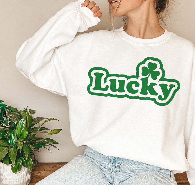 May include: White sweatshirt with a green shamrock and the word "Lucky" in a green retro font.