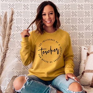 May include: A mustard yellow sweatshirt with a black circle graphic that reads "The influence of a good teacher can never be erased."