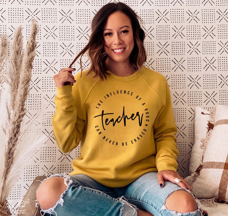May include: A mustard yellow sweatshirt with a black circle graphic that reads "The influence of a good teacher can never be erased."