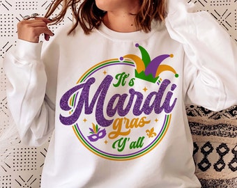Puede incluir: Sudadera blanca con un diseño de Mardi Gras morado, dorado y verde. El diseño presenta un gorro de bufón, las palabras "It's Mardi Gras Y'all" y una máscara morada.