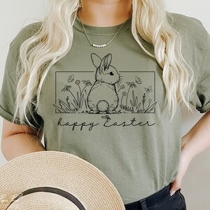 May include: A green t-shirt featuring a black line drawing of a bunny rabbit in a field of flowers. The text "happy Easter" is printed below the bunny.
