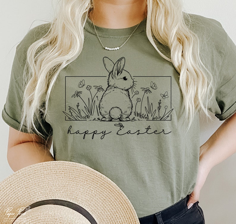 May include: A green t-shirt featuring a black line drawing of a bunny rabbit in a field of flowers. The text "happy Easter" is printed below the bunny.