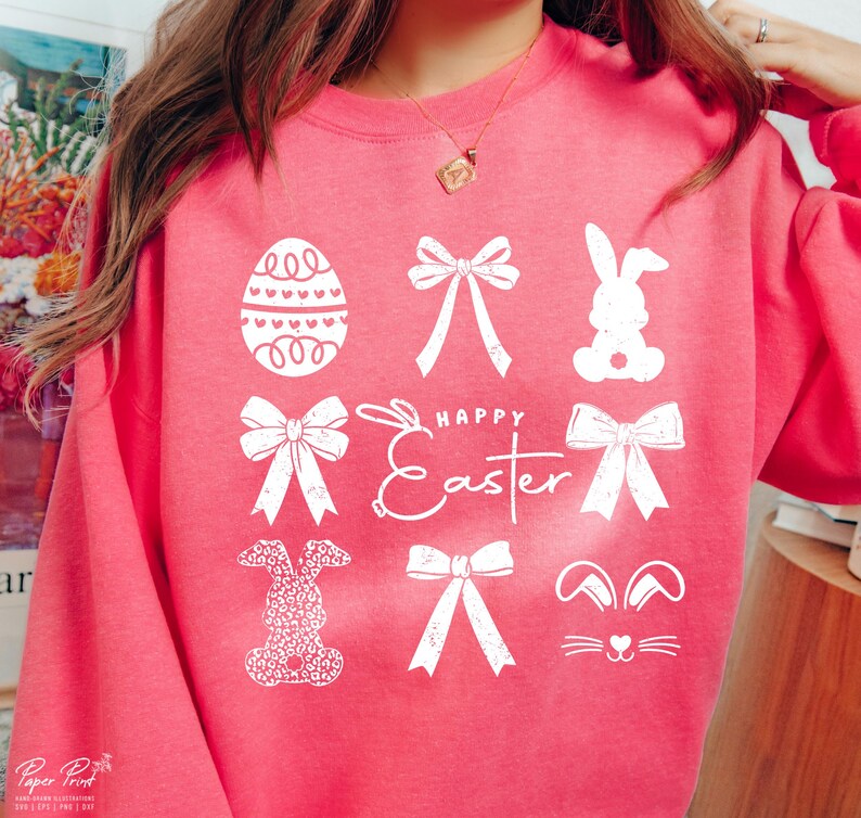 May include: Pink sweatshirt with a white graphic design featuring Easter-themed elements like bunnies, bows, and eggs. The text "Happy Easter" is also included in the design.