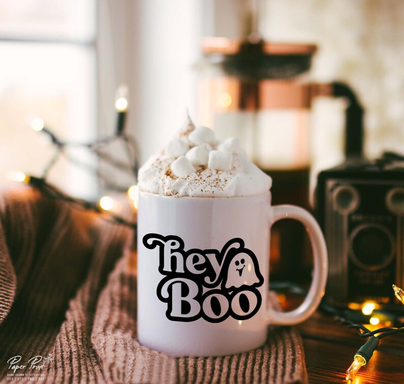 May include: White ceramic mug with a black graphic that says "Hey Boo" with a ghost illustration. The mug is filled with a hot beverage topped with whipped cream and marshmallows.