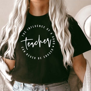 May include: Black t-shirt with a white circle graphic that says "The influence of a good teacher can never be erased".