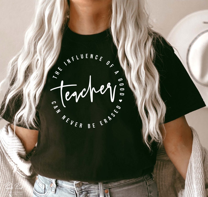 May include: Black t-shirt with a white circle graphic that says "The influence of a good teacher can never be erased".