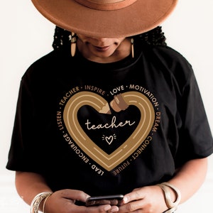 Pu&ograve; includere: Maglietta nera con una grafica a forma di cuore di matita marrone che dice "teacher" all'interno. La matita &egrave; disegnata in un cerchio con le parole "listen, teacher, inspire, love, motivation, dream, connect, future, lead, encourage" intorno al cuore.