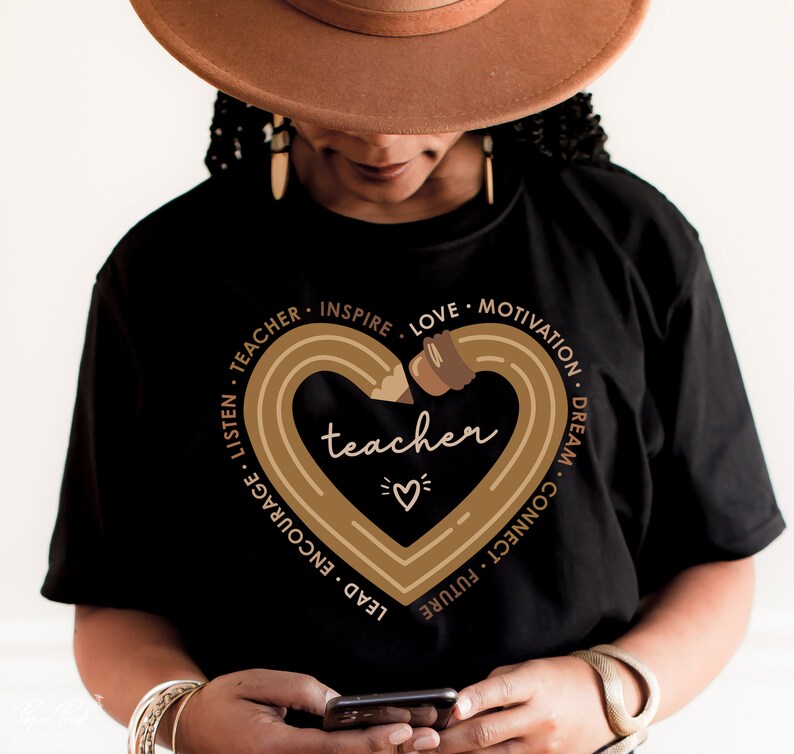 Pu&ograve; includere: Maglietta nera con una grafica a forma di cuore di matita marrone che dice "teacher" all'interno. La matita &egrave; disegnata in un cerchio con le parole "listen, teacher, inspire, love, motivation, dream, connect, future, lead, encourage" intorno al cuore.