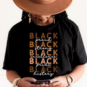 Op de afbeelding: Een zwart T-shirt met de woorden "BLACK proud BLACK strong BLACK excellence BLACK pride BLACK history" gedrukt in bruine en oranje letters.