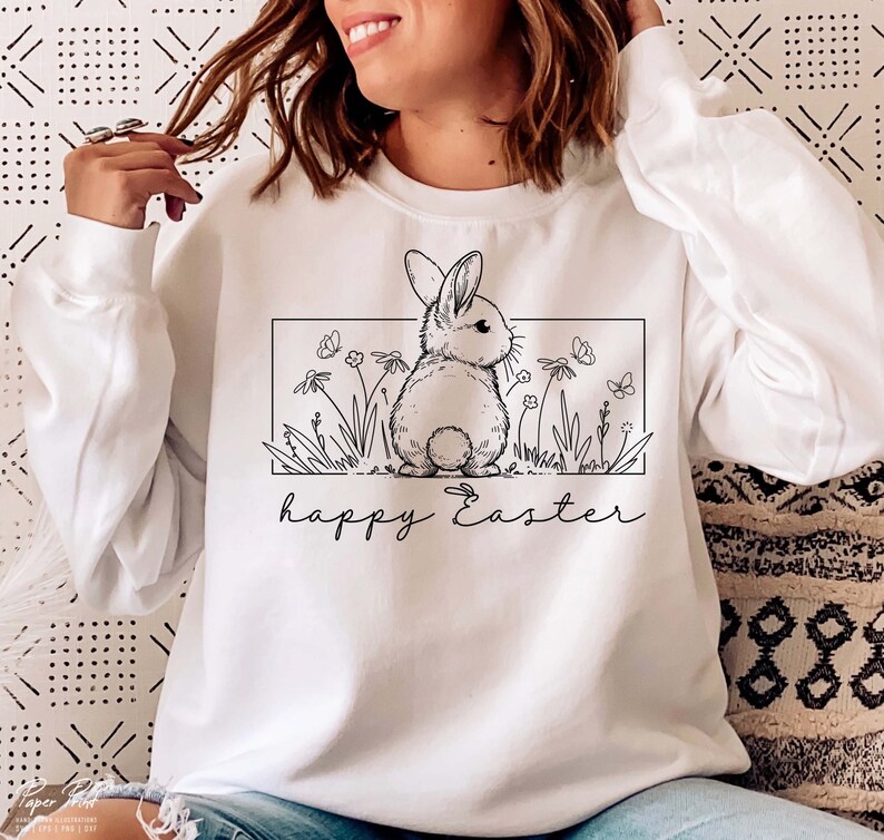 May include: White sweatshirt featuring a black and white illustration of a bunny rabbit in a field of flowers. The text "happy Easter" is printed below the illustration.