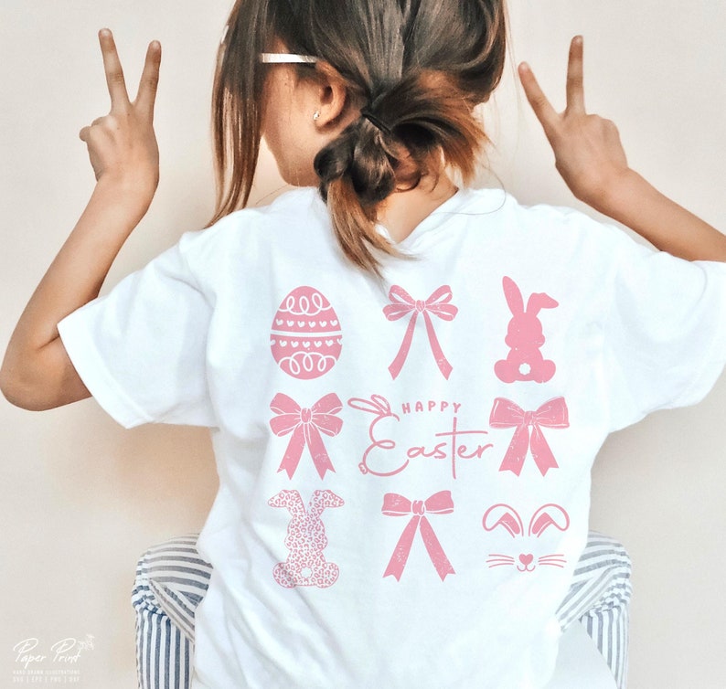 May include: White t-shirt with pink Easter-themed graphics. The graphics include a bunny, an egg, bows, and the text "Happy Easter".