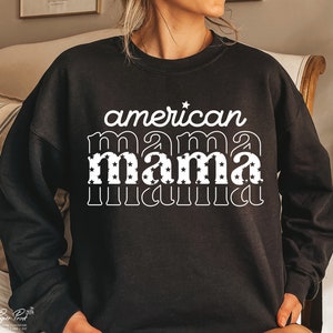 Pode incluir: Camisola de moletom preta com texto branco que diz "american mama" com a palavra "mama" em uma fonte retr&ocirc; e cheia de estrelas brancas.