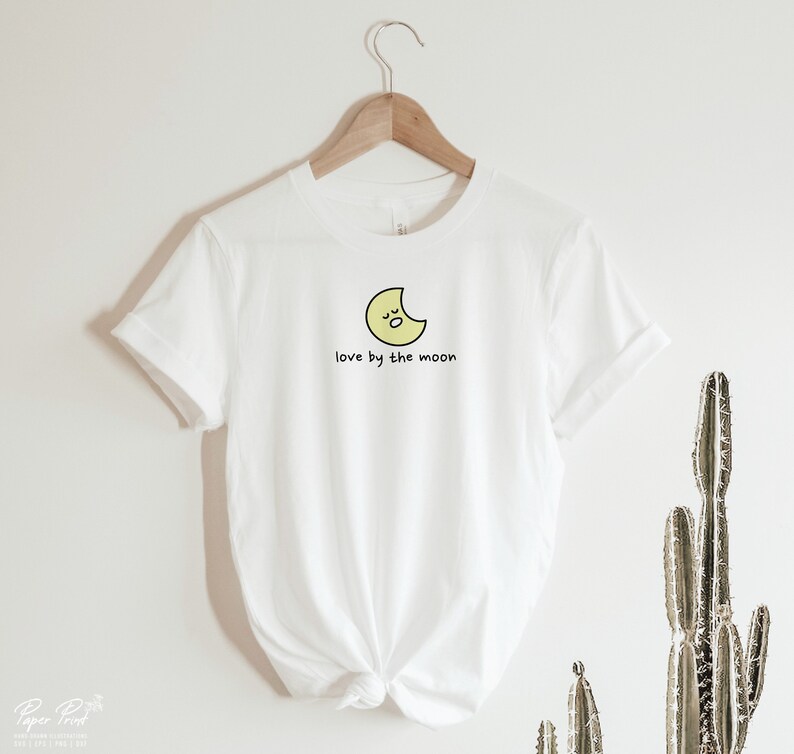 May include: White t-shirt with a yellow crescent moon graphic and the text "love by the moon".
