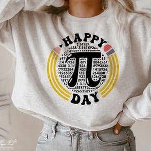 May include: A gray sweatshirt with a graphic design of a yellow and orange circle with the word "HAPPY" at the top and the word "DAY" at the bottom. Inside the circle is a large black pi symbol with numbers surrounding it.
