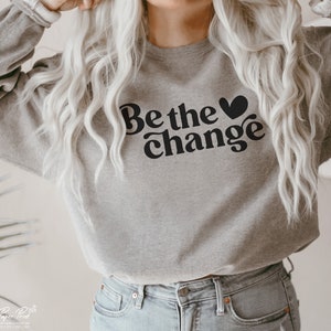 Puede incluir: Una sudadera gris con el texto "Be the &hearts; change" en negro.