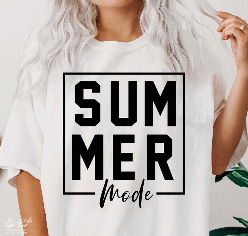 May include: A white t-shirt with the words "SUMMER MODE" in a black, bold, block font inside a black square. The word "Mode" is in a cursive font. The shirt is being worn by a person.