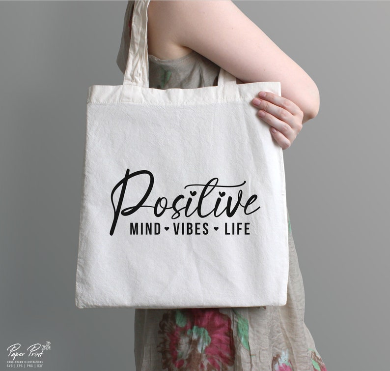 May include: A white canvas tote bag with black text that reads "Positive Mind Vibes Life".