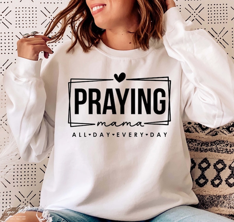 May include: White sweatshirt with black text that reads "Praying mama all day every day" with a heart symbol.