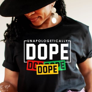 May include: A black t-shirt with the words "Unapologetically Dope" in white letters. The word "Dope" is repeated three times in smaller boxes with red, green, and yellow backgrounds.