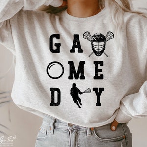 May include: A gray sweatshirt with the text "GAME DAY" in black with a lacrosse stick and helmet graphic.