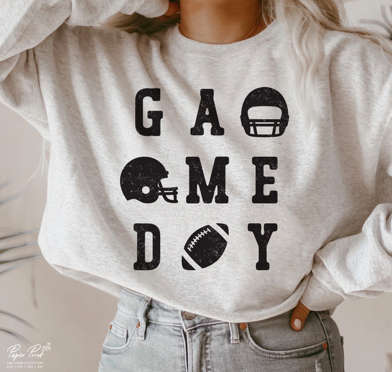 May include: A gray sweatshirt with the text "GAME DAY" in black block letters. The text is surrounded by images of football helmets and a football.