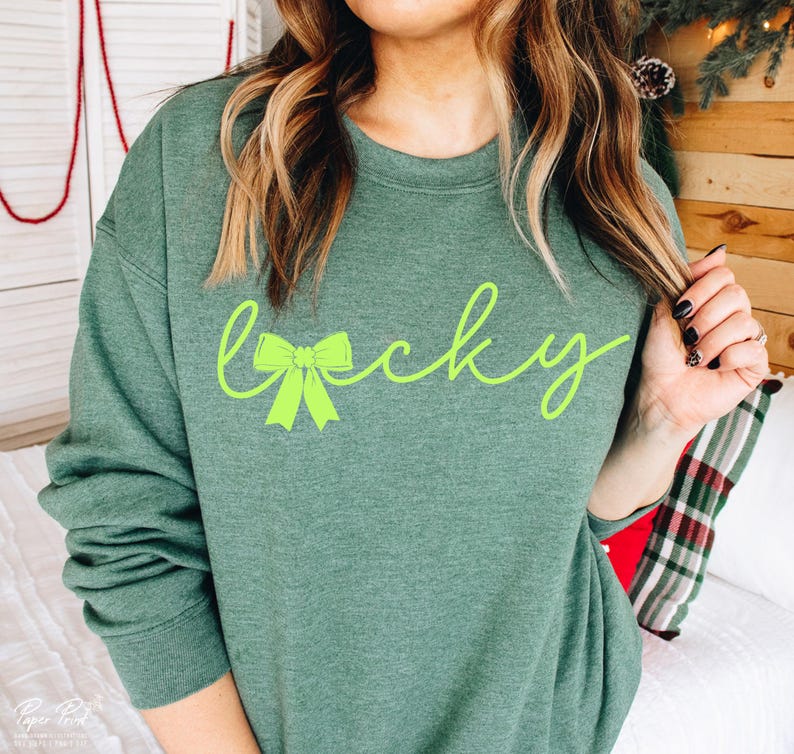 Puede incluir: Una sudadera verde con la palabra "lucky" escrita en letra cursiva con un lazo verde en el medio de la palabra.