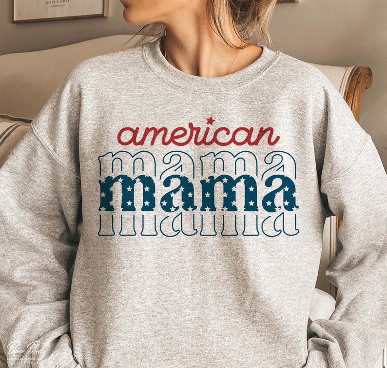 Pode incluir: Camisola cinzenta com o texto "american mama" em vermelho e azul com estrelas. O texto est&aacute; numa fonte retro.