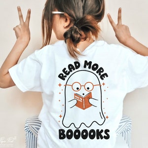 May include: White t-shirt with a ghost wearing glasses and reading a book that says "How to Boooks". The text on the shirt says "Read More Booooks".