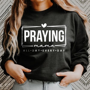 May include: Black sweatshirt with white text that reads "Praying mama all day every day" with a heart symbol between each word.