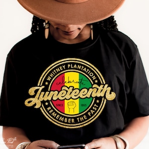 Puede incluir: Camiseta negra con un gráfico circular dorado que dice "Whitney Plantation - Celebrate Juneteenth - Since 1865 - Remember the Past". El gráfico tiene un esquema de color rojo, amarillo y verde.